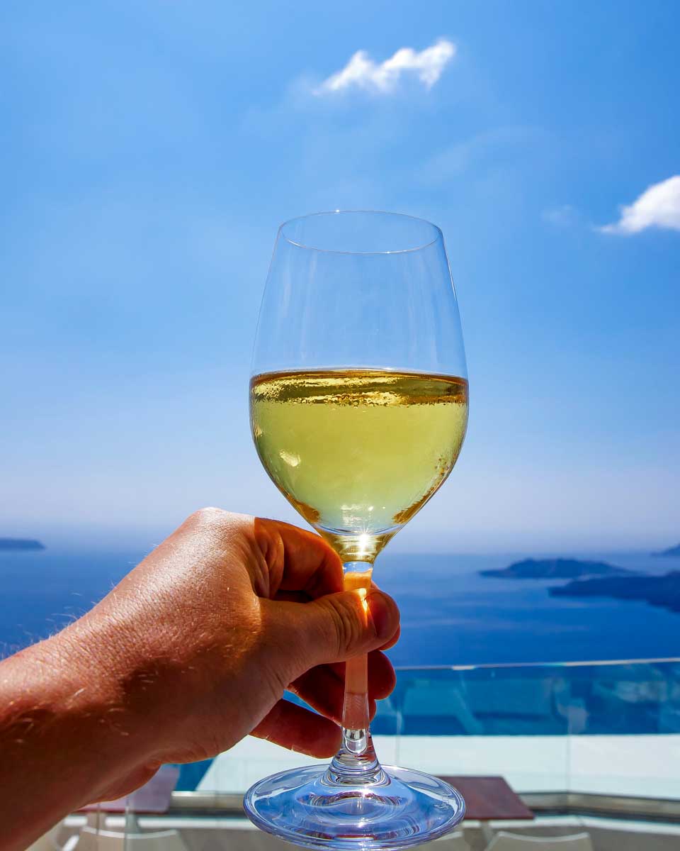A-person-holds-a-glass-of-wine-with-the-Aegean-Sea-in-the-background-on-a-tour-from-Santorini-Greece