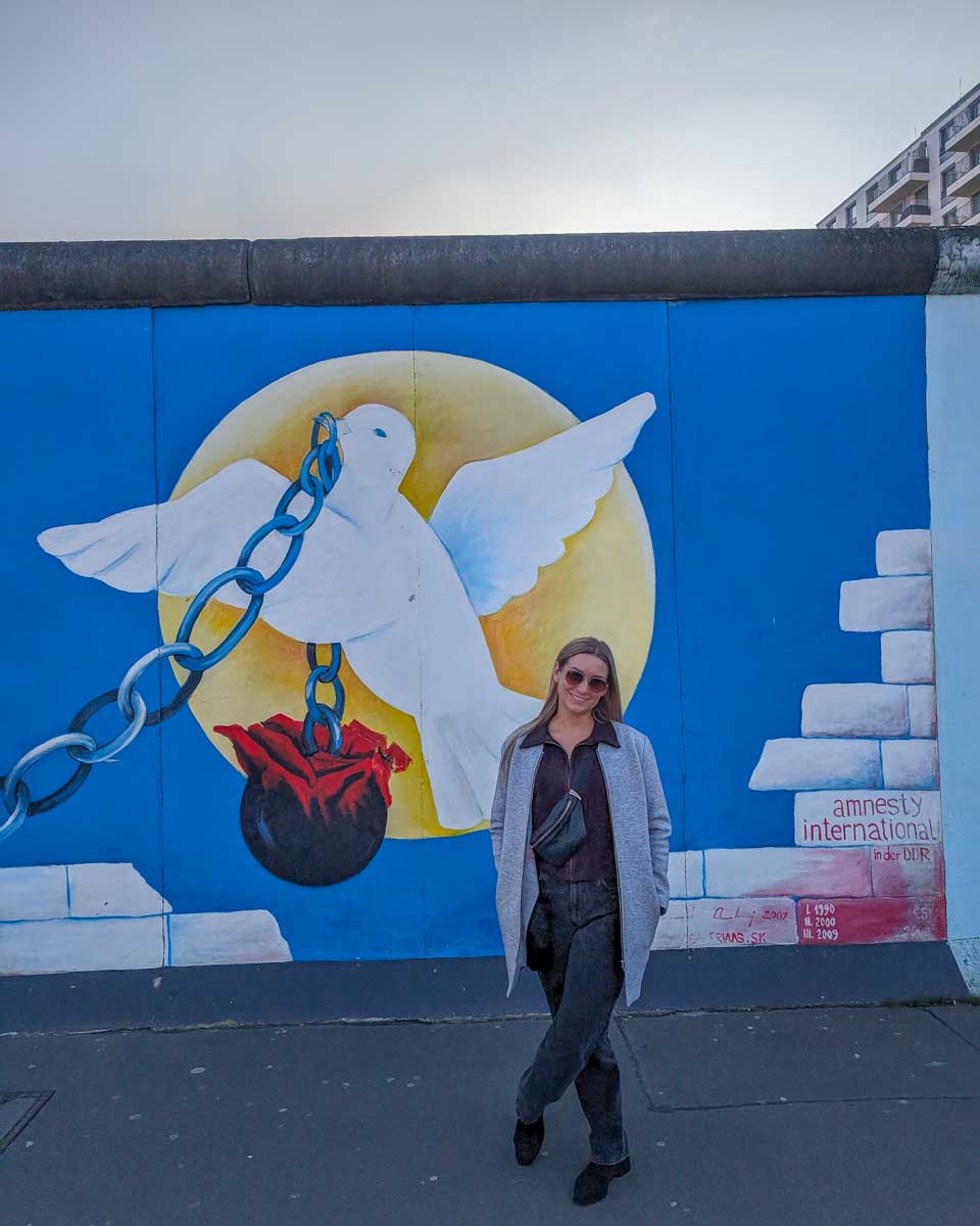Bailey-stands-with-street-art-of-a-doveEast Side Gallery-in-berlin-Germany