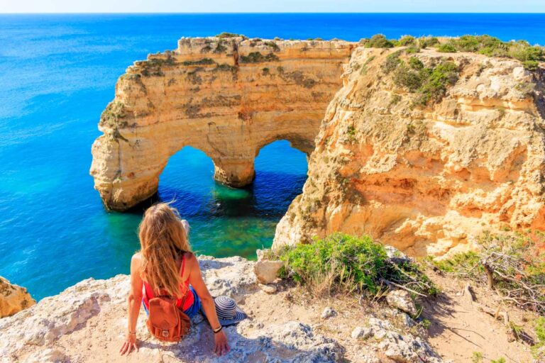 A woman sits at a rocl formation in Algarve Portugal